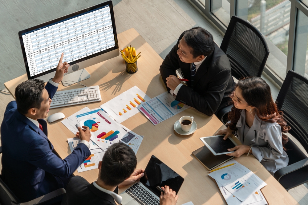 image of colleagues sitting at a table, working together with papers on the table and a computer